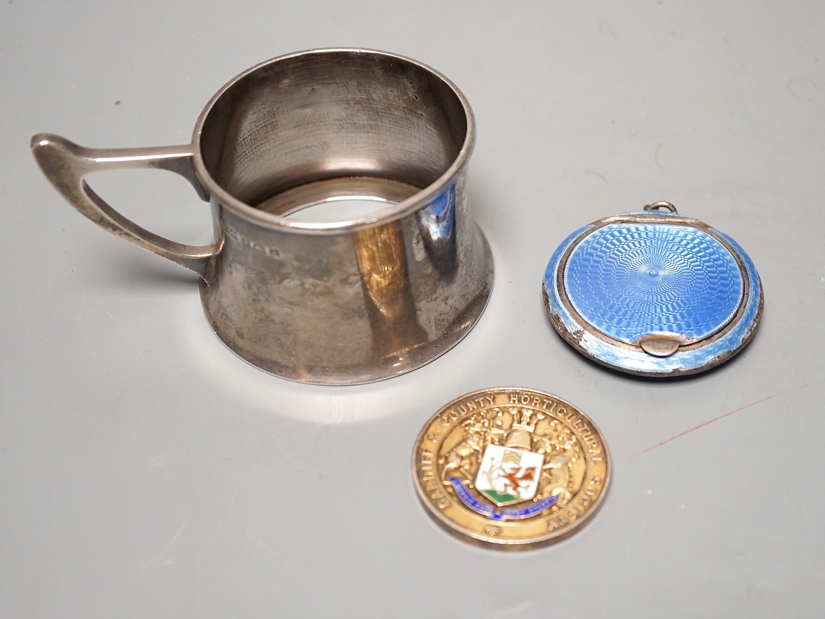 A George V silver cup holder, Birmingham, 1918, a silver and enamel Cardiff & County Horticultural Society medallion and a silver and enamel compact(a.f.0